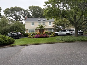 Colonial house with a densely planted, colorful round island bed of annuals, tropical foliage, and garden statuary by the front walk
